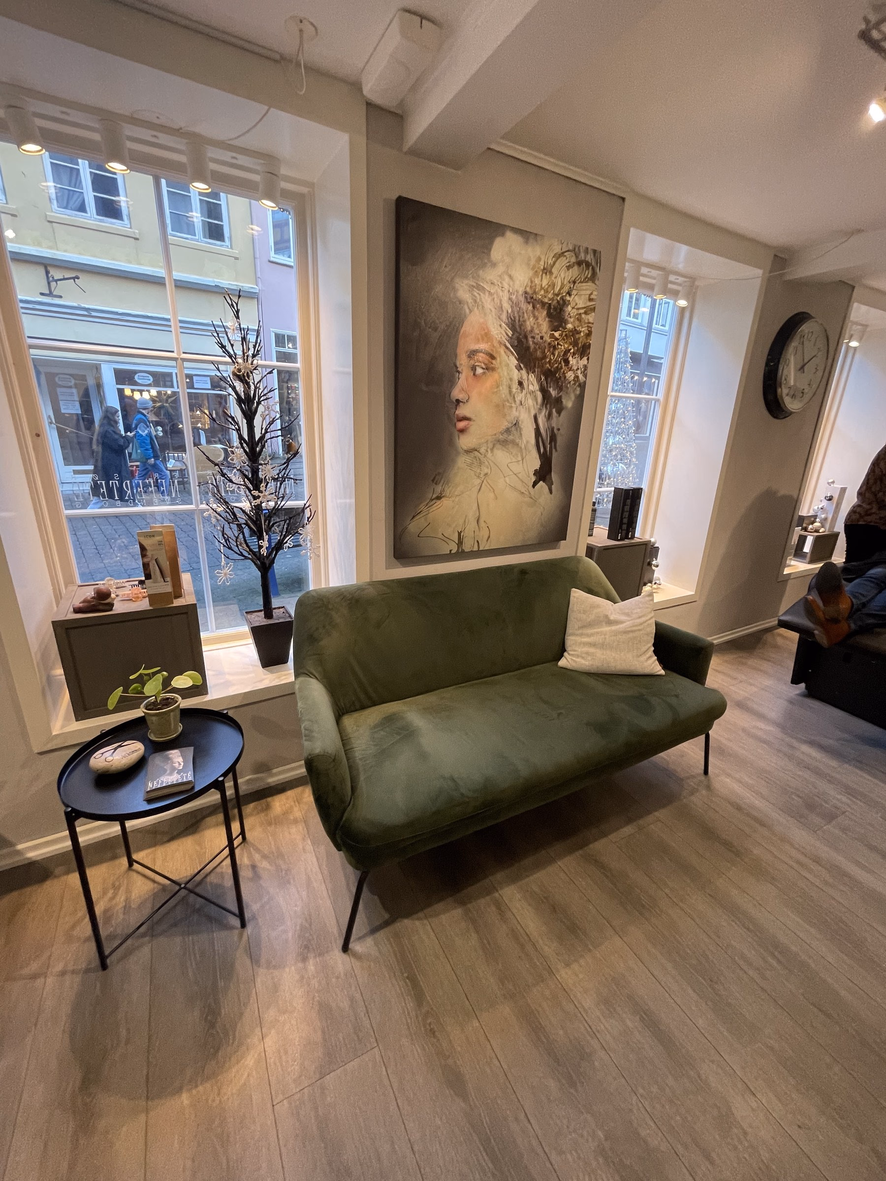 Loungezone hos Frisør Nefertete med grøn velour-sofa foran vinduet ud mod Møllergade — rummet hvor Stilletid finder sted